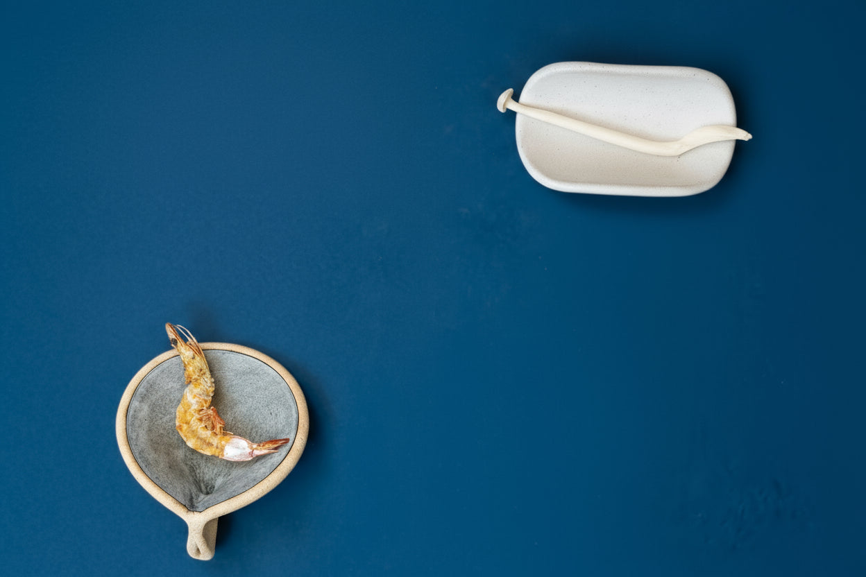 Handmade ceramic pinch and taco serving pieces displaying food, set on a cerulean blue background