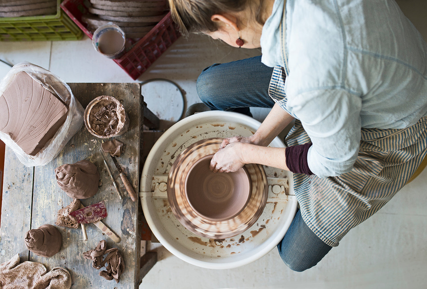 Ceramicist Wynne Noble carefully sculpting a bowl out of red clay on a throwing wheel