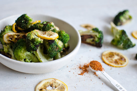 A white bowl full of broccoli seasoned with lemon moons and paprika