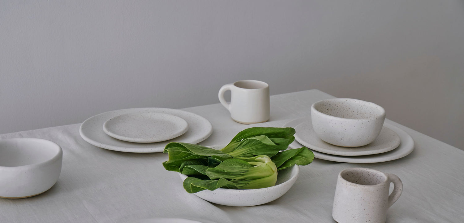 White table set with ivory-colored dishes and a bowl of crisp looking bok choy