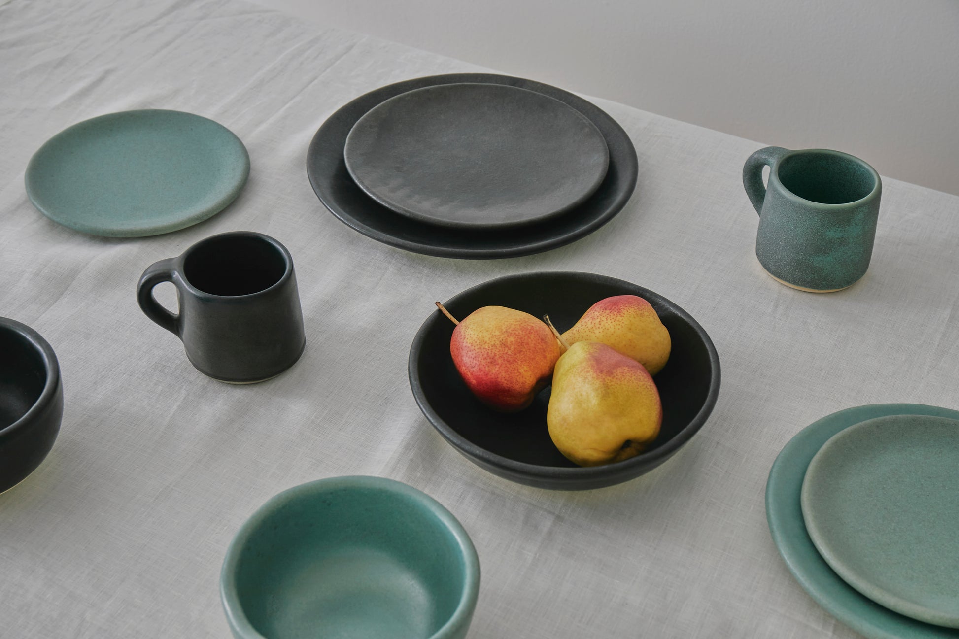 Table set with black and sage-colored dishes, centering a shallow bowl of orange and yellow pears
